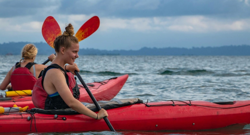 Two people wearing life jackets paddle red kayaks on open water